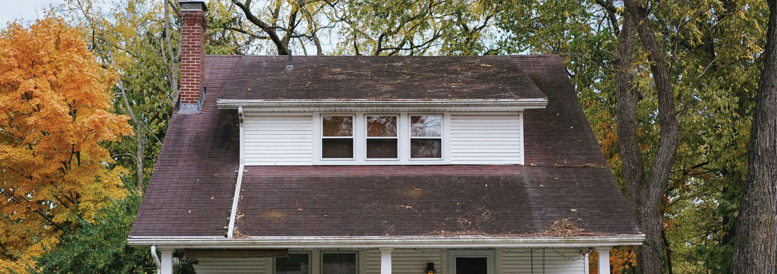 Wide view of an older, aged house roof featuring advanced weathering, organic staining, debris accumulation, and compromised shingle transitions in Cincinnati.