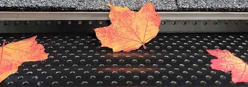 Black aluminum Shur Flo gutter guard sitting in gutter preventing leaves from entering channel.