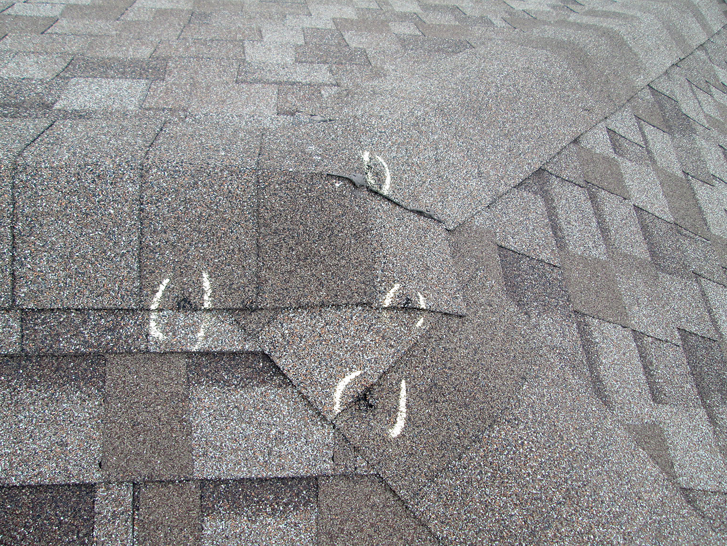 Close-up of roof shingles marked with white chalk to highlight impact bruises from hail damage.