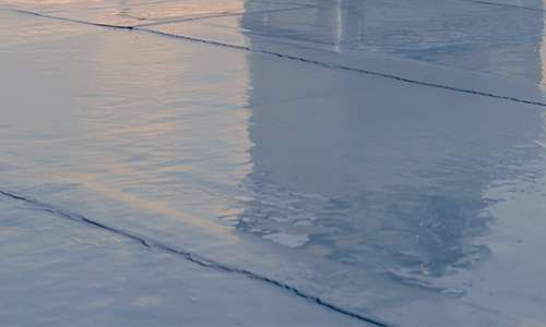 Close-up view of a smooth, glossy dark EPDM synthetic rubber membrane installation covering a flat commercial rooftop.