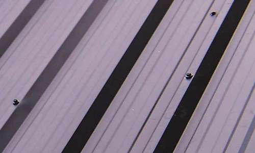 Close-up view of ribbed metal roofing panels with visible exposed hex screws installed on a commercial building structure.