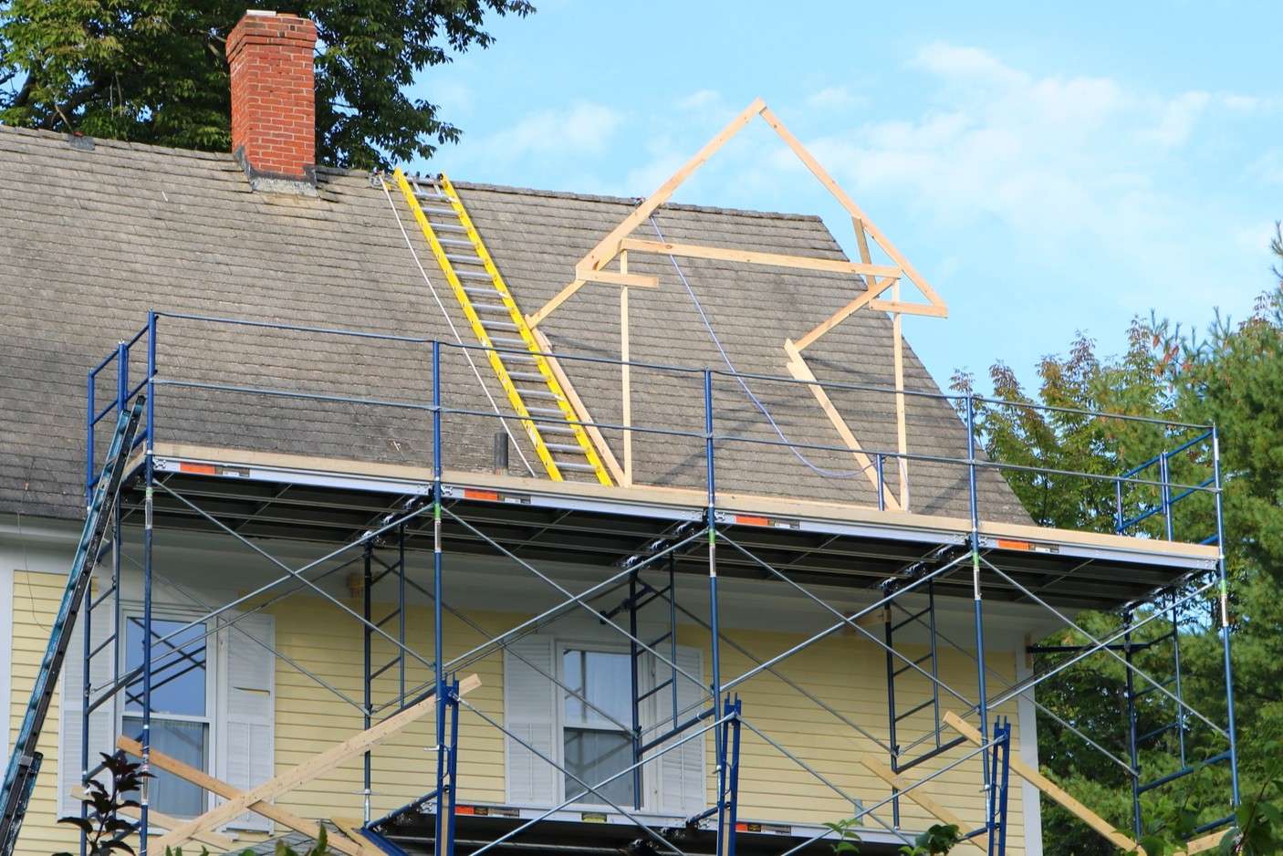 An educational slider panel titled After Other Improvements showcasing a yellow residential house wrapped in heavy metal construction scaffolding and structural wood framing accents during an exterior home improvement project.