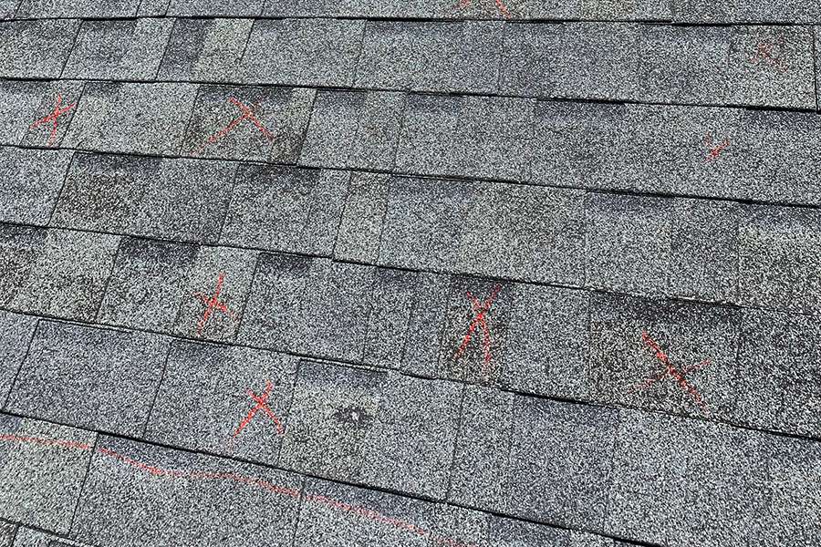 An educational module graphic showing a weathered asphalt shingle roof with several compromised areas marked in red chalk, indicating hidden soft spots and rotted wood decking beneath the surface.