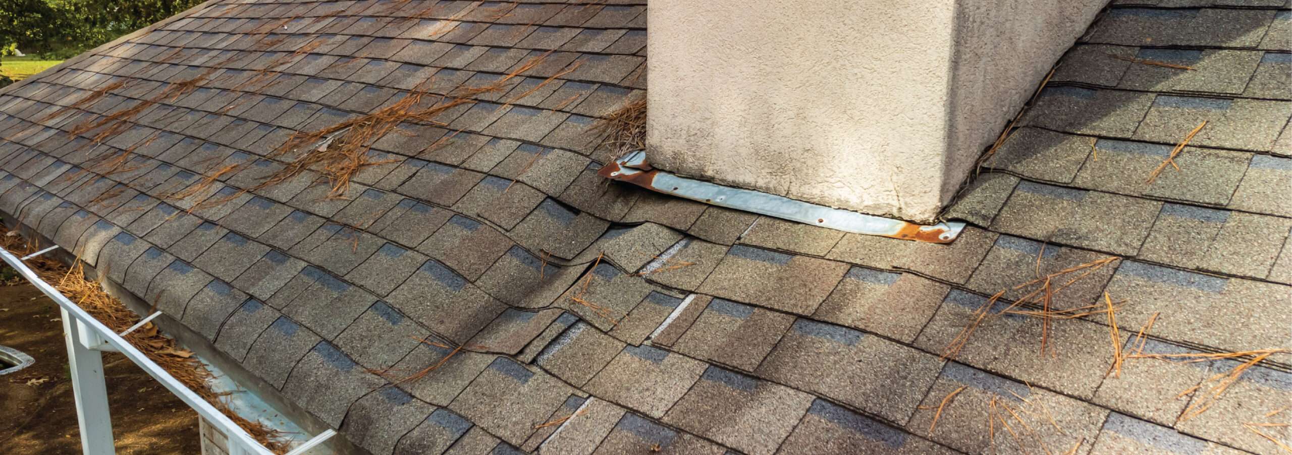 Close-up of a rotting and sagging roof deck structure with warped shingles and rusted metal flashing next to a stucco chimney in Cincinnati.