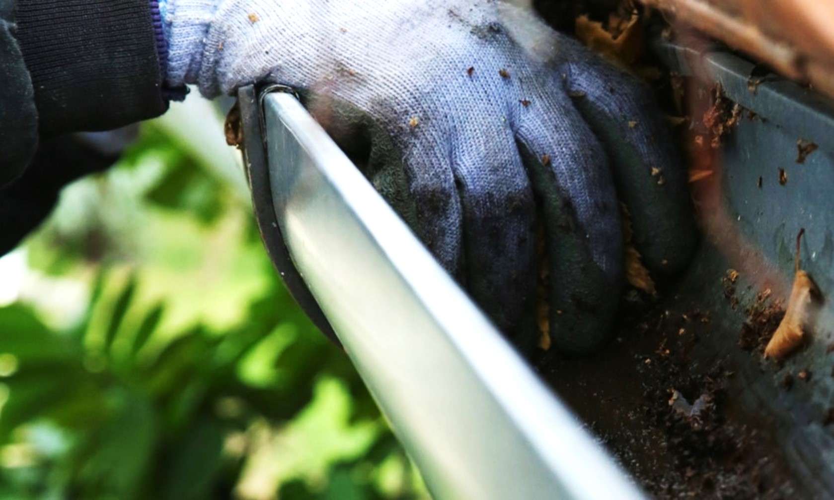 An educational slider graphic titled Proactive Asset Maintenance displaying a close-up view of a gloved hand clearing leaves and organic debris from a residential aluminum gutter trough.