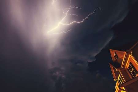 An educational slider graphic titled Strategic Milestones and External Triggers showing a dramatic night sky with a lightning bolt striking over the roofline of a residential building during a severe storm event.