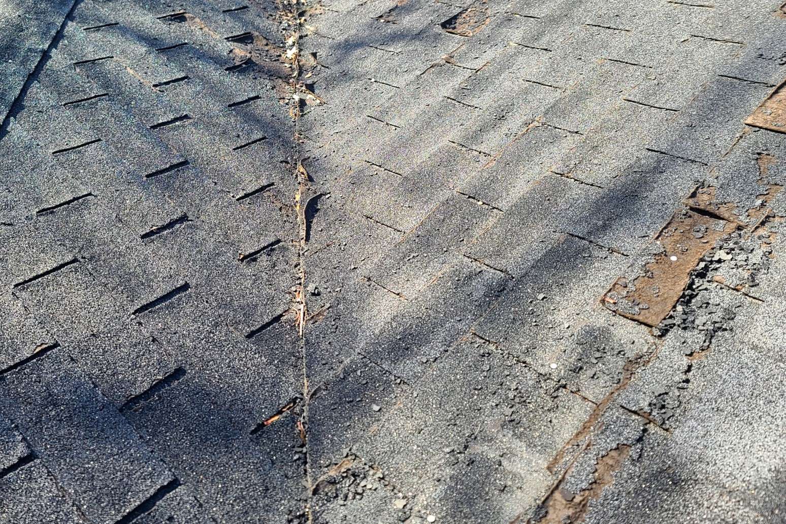 An educational slider image displaying an up-close section of an aging roof facet with heavy bald patches and extensive mineral granule loss across the weathered shingle surfaces.