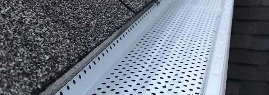 Silver aluminum gutter guard sitting within gutter channel at edge of roof line.